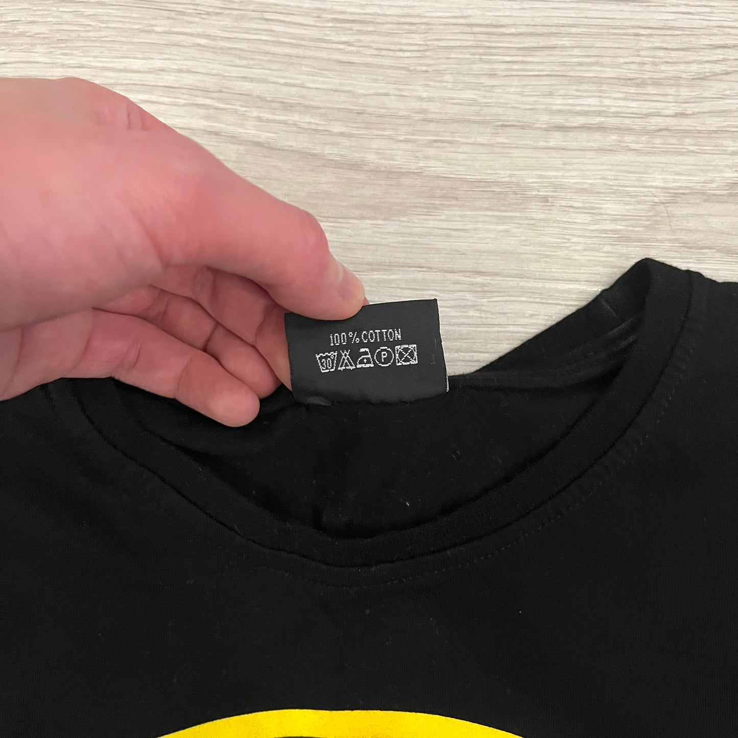 Glock Safe Action Pistol T-Shirt in black, made on an Orijin blank from 100% cotton. Features a large Glock pistol graphic on the front set inside a yellow circle, with “Glock Safe Action” text and Glock logo running around the graphic. The back has a white Glock logo printed below the collar. 