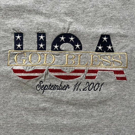 Gray “God Bless USA” tee on an Alstyle blank, made from soft, durable cotton. Embroidery showcases USA in flag colors with gold “God Bless” text and a subtle September 11, 2001 detail underneath. A respectful and collectible commemorative shirt.