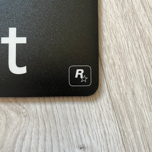 Official Rockstar Games Grand Theft Auto V "iFruit" Mouse Pad. Sleek black hard-plastic surface with a smooth, low-friction finish and the classic iFruit logo in color. Features a durable non-slip rubber base for stability and the Rockstar Games logo at the bottom. Originally available via the Rockstar Warehouse during GTAV’s release period.