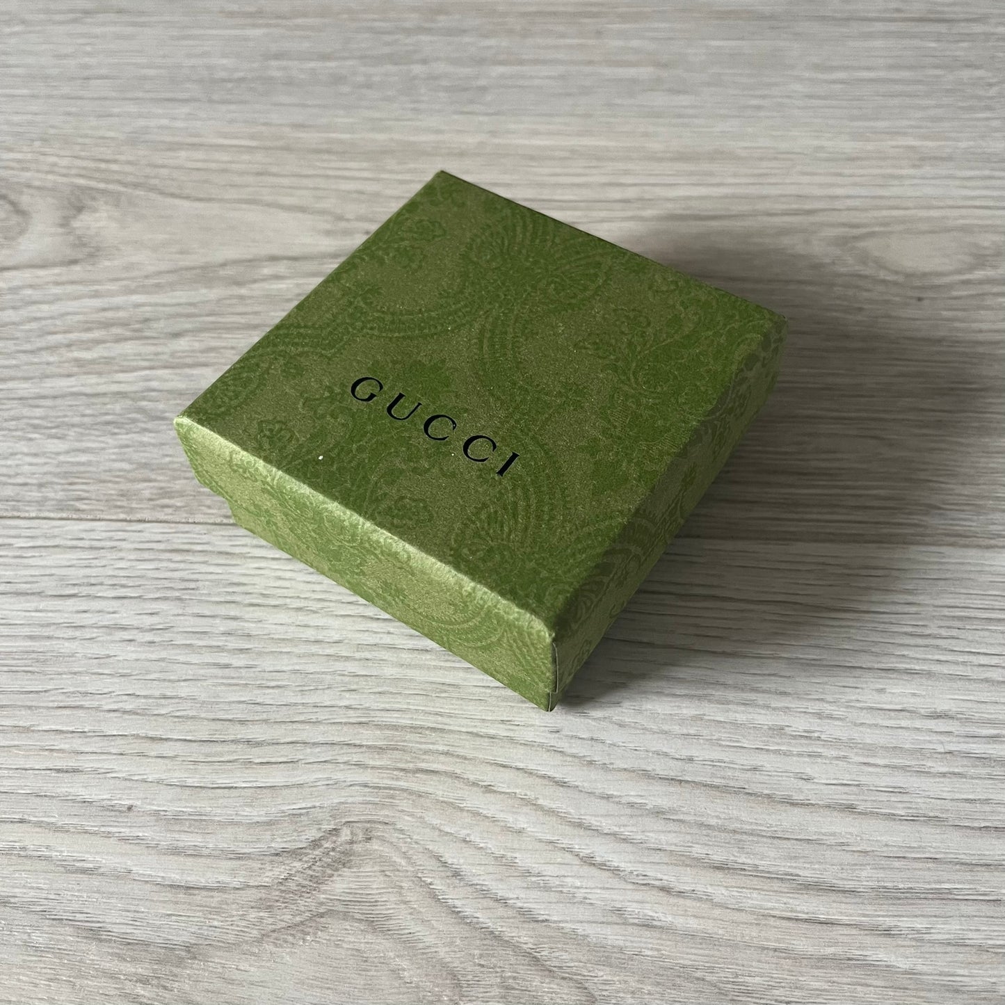 Green Gucci jewelry box on a wooden surface