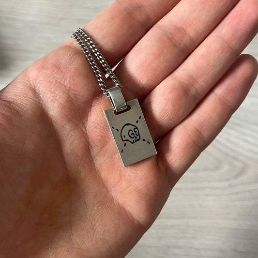 Hand holding a silver pendant with a skull design on a neutral background