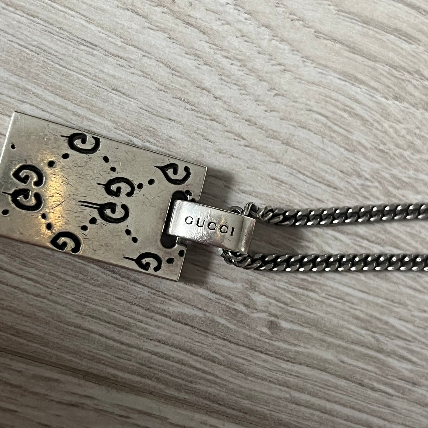 Silver Gucci necklace with a rectangular tag on a wooden surface