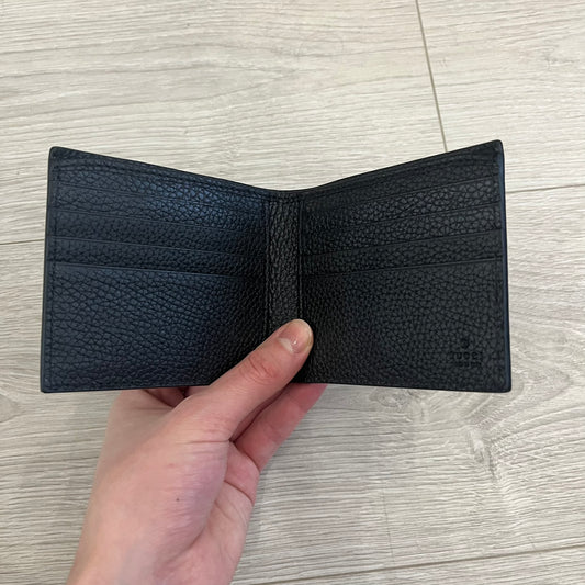 Gucci Jumbo GG Bi-Fold Leather Wallet in black calfskin, featuring the brand’s iconic debossed Jumbo GG logo. This Italian-made wallet offers eight card slots, two bill compartments, and a bi-fold design for organized storage. Finished with grained leather and a moiré lining.