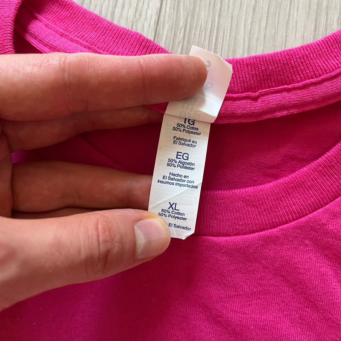 Hand holding a pink garment with a label showing size and material details.