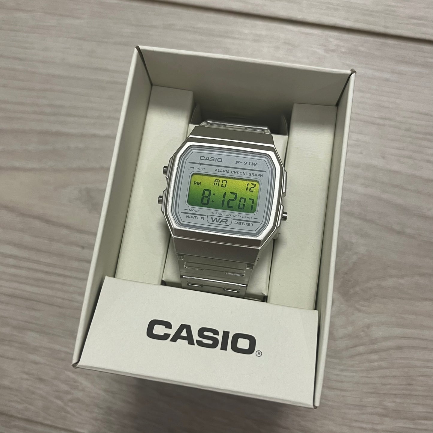 Digital watch in a Casio packaging box on a wooden surface.