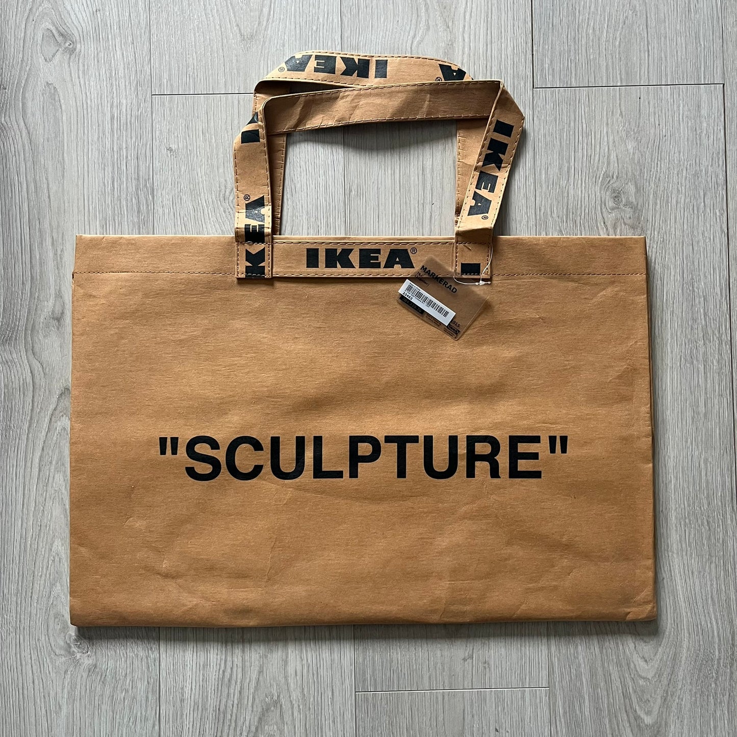 Ikea x Virgil Abloh Markerad "Sculpture" Carrier Bag from FW19 reimagines the iconic blue Frakta tote in reinforced brown paper. Embellished with Abloh’s signature quotation marks, the “SCULPTURE” print transforms a utilitarian object into conceptual design. A collectible symbol of functional art and everyday irony.