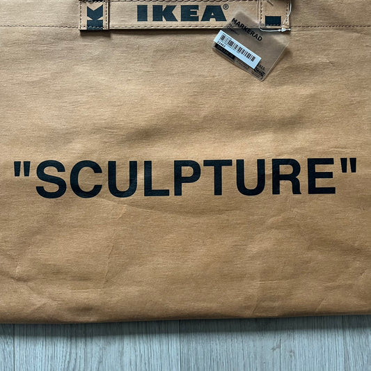 Ikea x Virgil Abloh Markerad "Sculpture" Carrier Bag from FW19 reimagines the iconic blue Frakta tote in reinforced brown paper. Embellished with Abloh’s signature quotation marks, the “SCULPTURE” print transforms a utilitarian object into conceptual design. A collectible symbol of functional art and everyday irony.