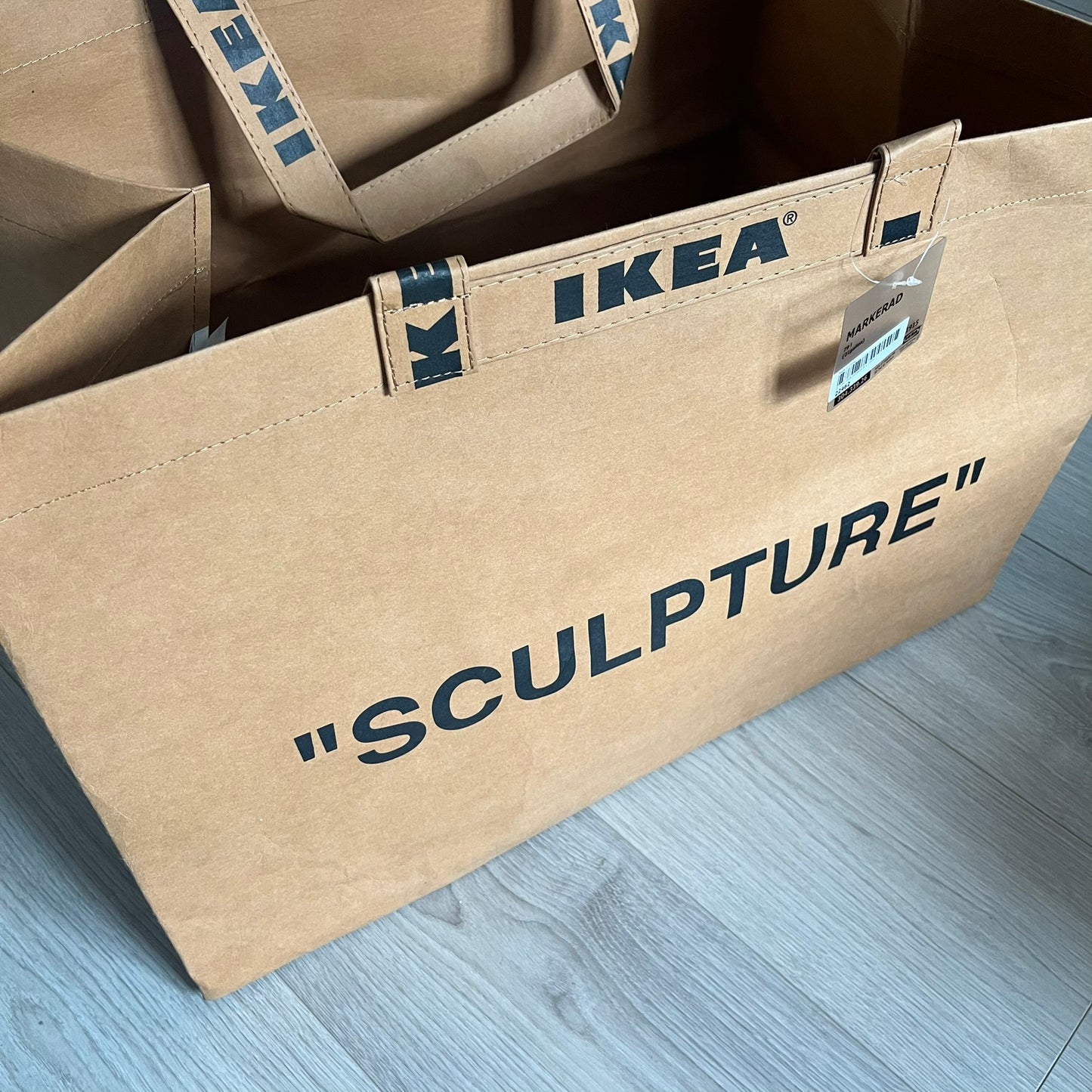 Ikea x Virgil Abloh Markerad "Sculpture" Carrier Bag from FW19 reimagines the iconic blue Frakta tote in reinforced brown paper. Embellished with Abloh’s signature quotation marks, the “SCULPTURE” print transforms a utilitarian object into conceptual design. A collectible symbol of functional art and everyday irony.