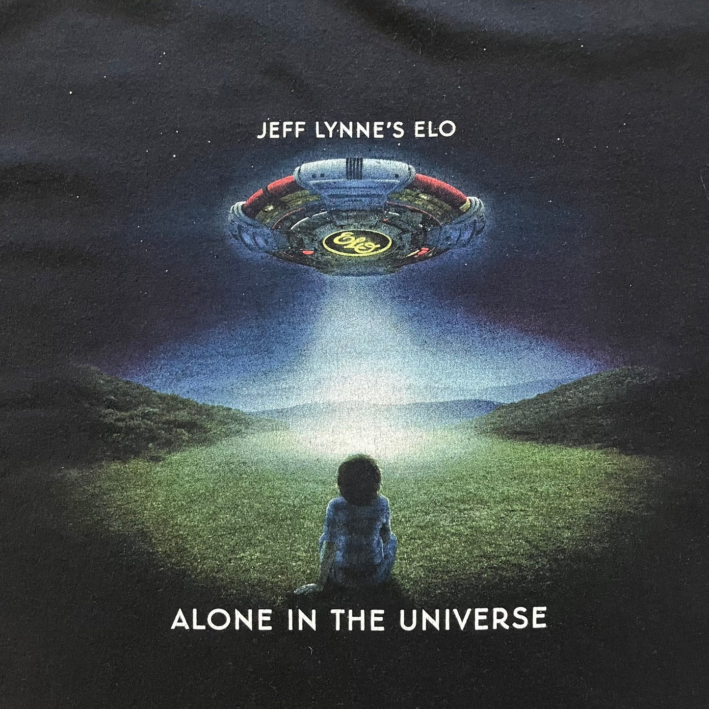 Official tour tee from Jeff Lynne’s Alone in the Universe era, released in 2015. The shirt comes in black with the album artwork printed on the front, while the back lists the 2015/2016 tour stops including London, Amsterdam, and Oberhausen