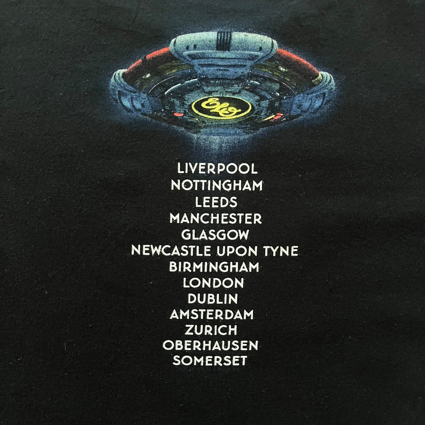 Official tour tee from Jeff Lynne’s Alone in the Universe era, released in 2015. The shirt comes in black with the album artwork printed on the front, while the back lists the 2015/2016 tour stops including London, Amsterdam, and Oberhausen