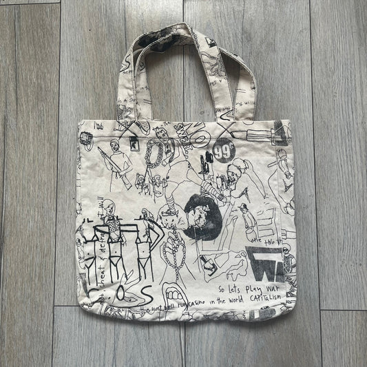 Jeremy Scott 2004 Chicks on Speed: It’s a Project Tote Bag is a cream canvas tote featuring multiple black hand-drawn style graphics including symbols, objects, and abstract motifs such as text elements, crossed-out luxury references, lips, watches, chains, and figures. The bag was originally part of a limited art publication kit released in 2004. It came with additional included items such as a book, poster, CD, clothing pattern, and fabric components as part of the full “Chicks on Speed: It’s a Project” s