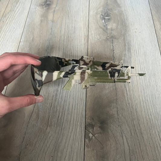 Jeremy Scott x Linda Farrow SS2013 Green Camo M16 Rifle Sunglasses (JSARMYC3SUN) are a statement eyewear piece from the Spring/Summer 2013 collaboration. The design features full camo green, brown, and beige frames with dark lenses, while the arms are constructed as detailed 3D M16 rifle shapes extending toward the front of the frame. The model includes Jeremy Scott branding on the inner arms and is produced in a high-detail acetate construction.