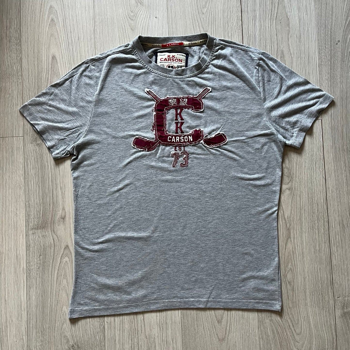Gray t-shirt with a red logo on a wooden floor