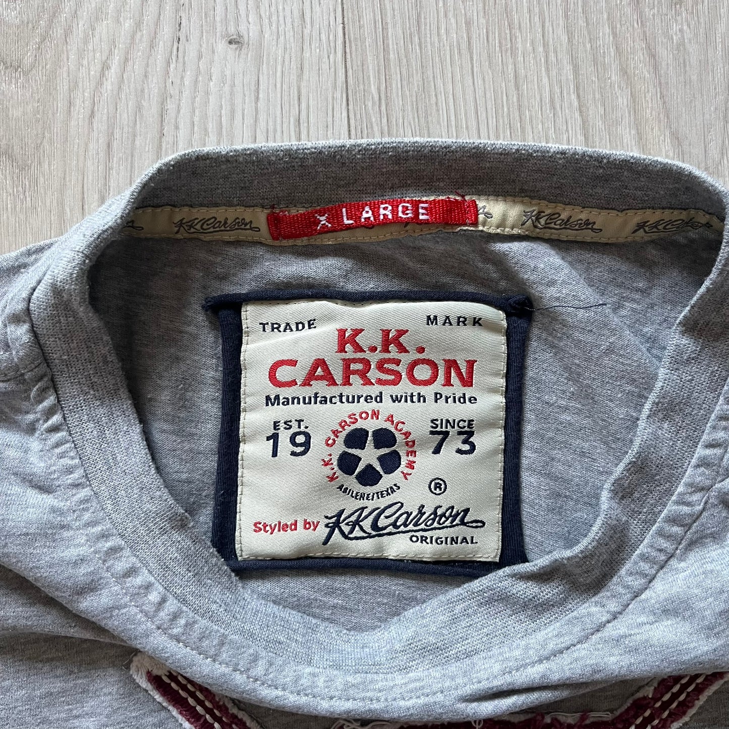 Gray shirt with K.K. Carson label on a wooden surface