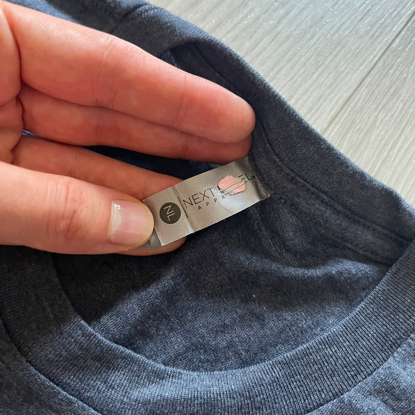 Hand holding a clothing tag on a gray garment