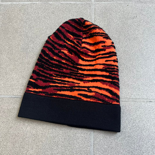 Kenzo x H&M Orange Tiger Camo Beanie is a knit beanie from the 2016 collaboration. It features an all-over tiger camouflage pattern in red, orange, and dark red tones, woven directly into the fabric. The design is finished with a black cuff and can be worn either slouched or folded for a more traditional beanie fit.