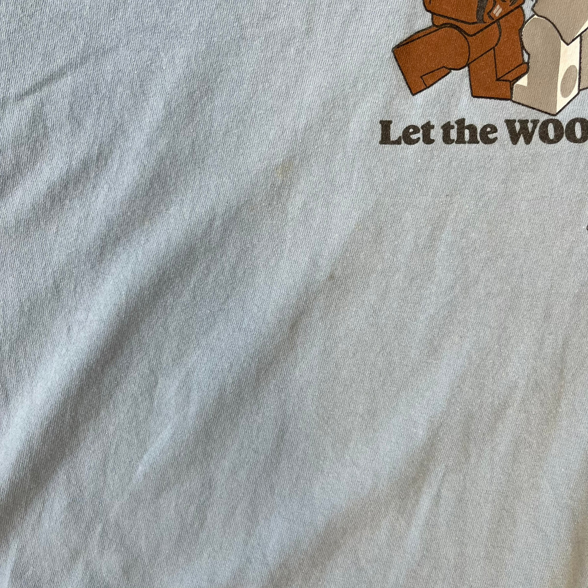 LEGO Star Wars 2007 “Let the WOOKIEE win!” Tee is a light blue, 100% cotton T-shirt with a front graphic of LEGO Chewbacca and two Stormtroopers, with Chewbacca holding the hands of one while the other stands to the side with a blaster. “Let the Wookiee win” text sits below the graphic, along with a small LEGO Star Wars logo and 2007 licensing. It has a Star Wars neck tag.