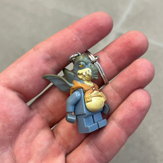 LEGO Star Wars 853413 Watto Key Chain is a 2012 LEGO Gear accessory featuring an authentic LEGO Watto minifigure attached to a metal key ring and chain. The Watto figure is permanently fixed to the chain and cannot be removed. The design represents Watto, the Toydarian junk dealer character from Star Wars: The Phantom Menace.