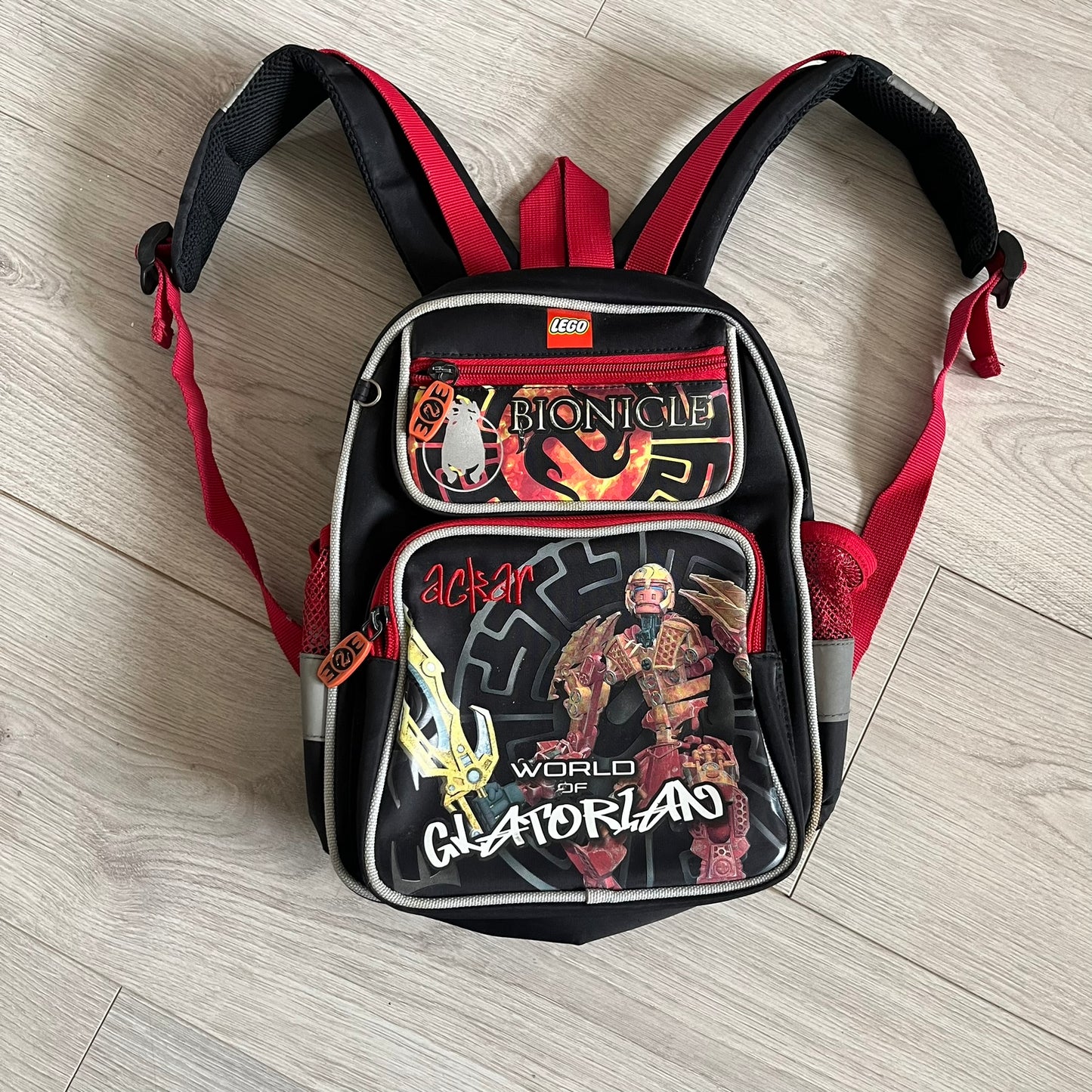 Lego Bionicle 2010 Glatorian Gresh Backpack made by Class Investment in 2010, featuring a front pocket with an embroidered Glatorian Ackar figure and text. The top pocket includes both Bionicle and LEGO logos, along with custom rubber zipper pulls. Finished with two side bottle pockets and additional Bionicle logo details, making it a great rare collectible for fans of the series.