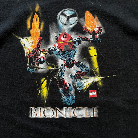 Rare 2000s Lego Bionicle T-shirt showcasing Toa Hordika Vakama from the 2005 set. Features the glowing Bionicle logo under the Binicle, small Lego branding and a naturally sunfaded black wash. A collectible tee that perfectly captures early-2000s nostalgia.