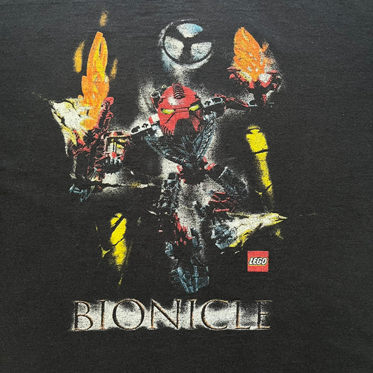 Rare 2000s Lego Bionicle T-shirt showcasing Toa Hordika Vakama from the 2005 set. Features the glowing Bionicle logo under the Binicle, small Lego branding and a naturally sunfaded black wash. A collectible tee that perfectly captures early-2000s nostalgia.