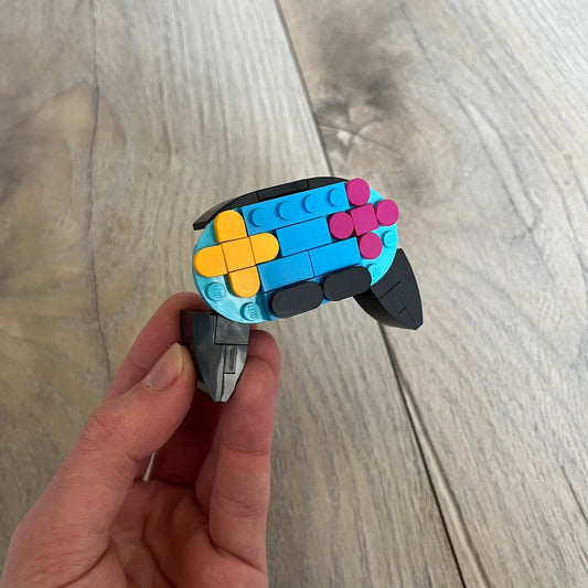 LEGO Controller Make and Take Build is a limited promotional LEGO set distributed as an exclusive “make & take” event and not available for retail purchase. The model features a small controller build in blue and black, with yellow and pink button elements.