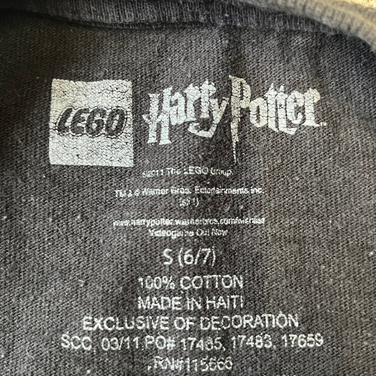 Lego Harry Potter: Years 1-4 Game 2011 Cover Tee is a black kids' T-shirt made from 100% cotton, featuring the game's cover artwork with classic characters and the Lego Harry Potter logo on the front. It carries a licensed 2011 Warner Bros. neck tag.