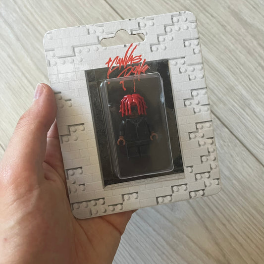 Lego Playboi Carti “Whole Lotta Red” minifigure featuring the Carti with red dreads from the album era. The figure is displayed on a paper/cartboard display accompanied by a small plate of the Lego style album cover, a limited addition only for first orders. A collectible piece from TheCanvasDon.