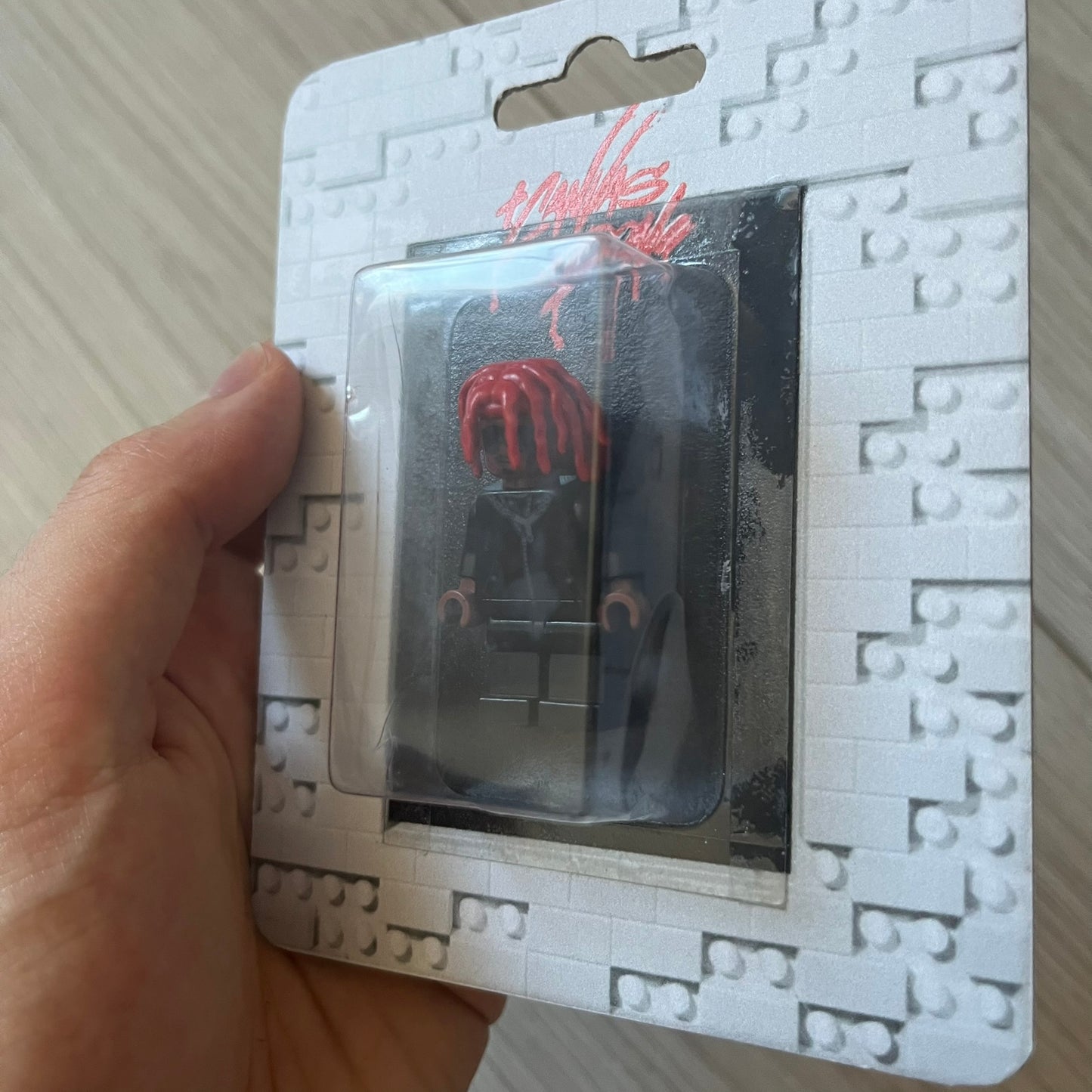 Lego Playboi Carti “Whole Lotta Red” minifigure featuring the Carti with red dreads from the album era. The figure is displayed on a paper/cartboard display accompanied by a small plate of the Lego style album cover, a limited addition only for first orders. A collectible piece from TheCanvasDon.
