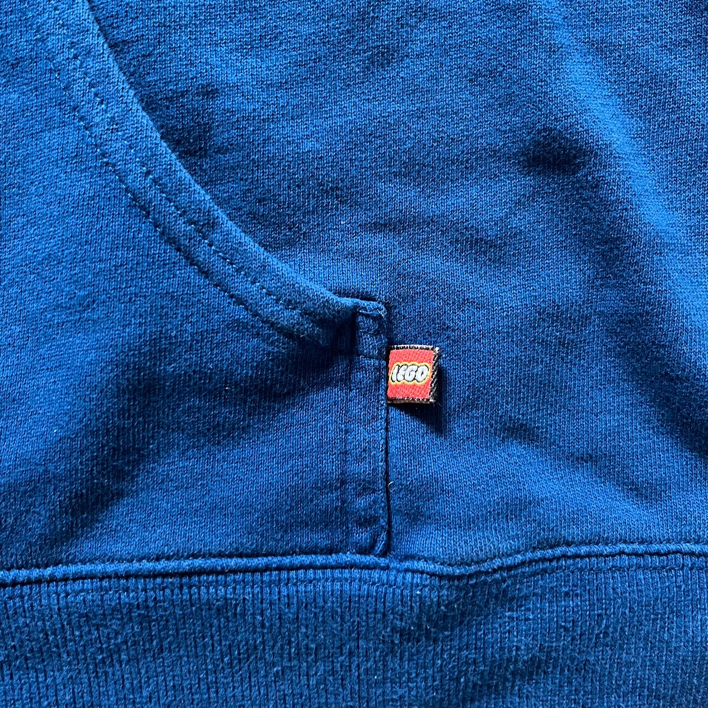 Lego Rainbow Minifigures Blue Hoodie from 2010, officially licensed by the Lego Group. Crafted from 100% cotton, it features seven colorful Lego minifigures in motion across the chest and a single red figure waving on the upper back. Designed in a bright blue colorway with a small Lego tag by the front pocket.