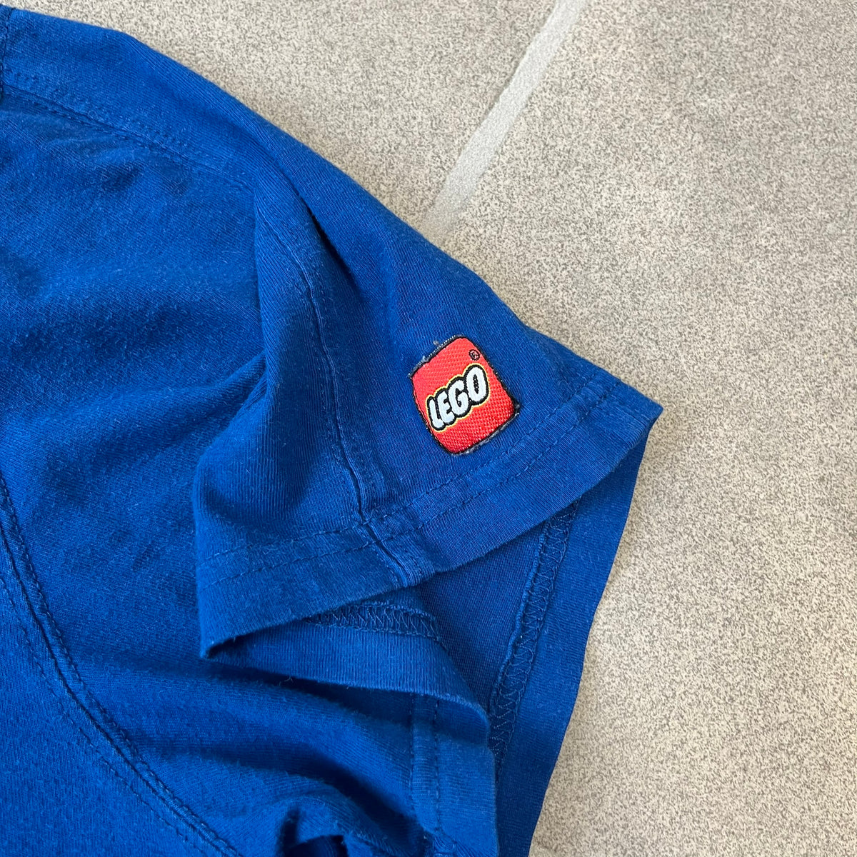 Lego Rainbow Minifigures Blue Tee from 2010, officially licensed by the Lego Group. Crafted from 100% cotton, it features seven colorful Lego minifigures in motion across the chest. Designed in a blue colorway with a small Lego tag on the left sleeve.