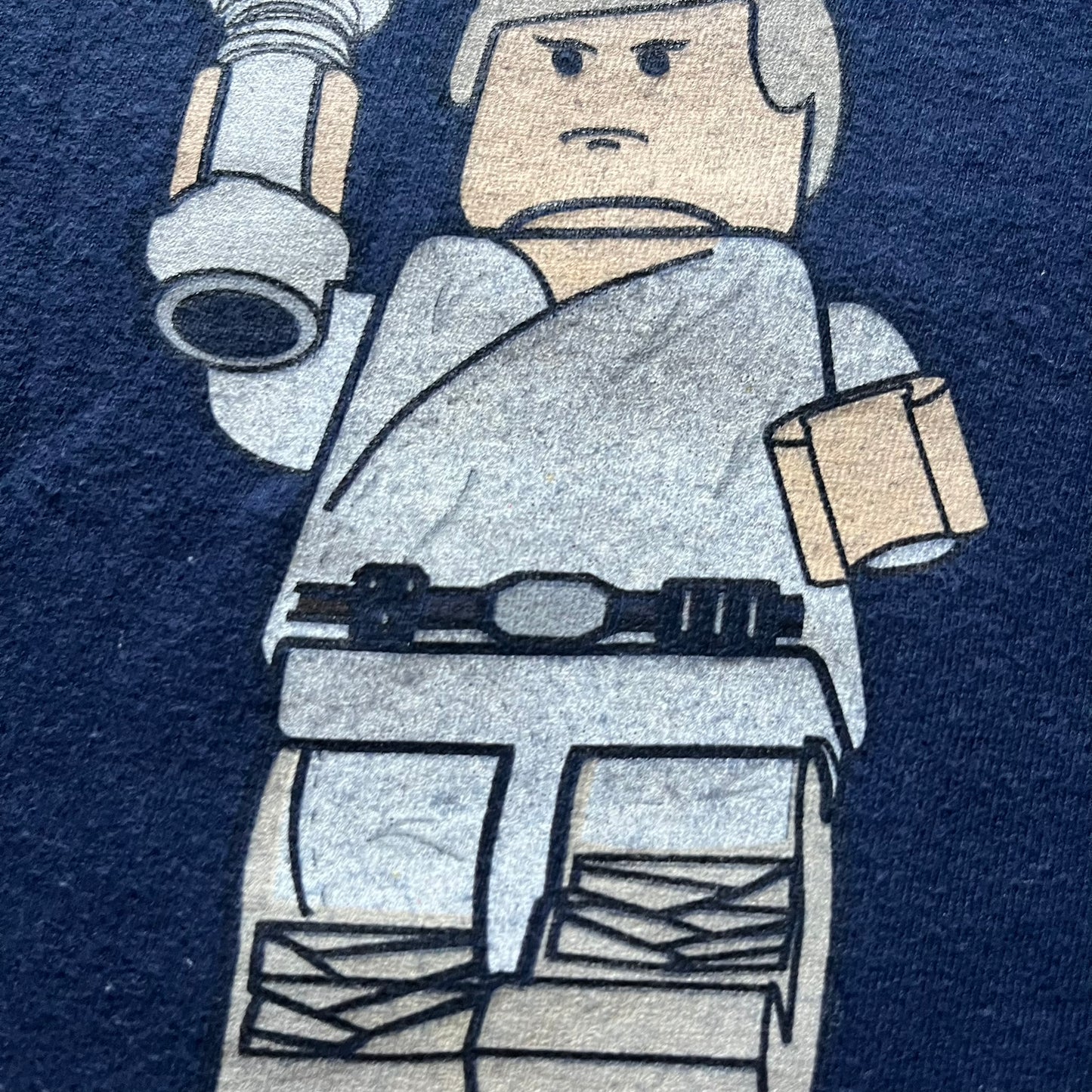 Vintage 2007 Lego Star Wars tee featuring Luke Skywalker with a lightsaber and the quote “I am a Jedi like my father before me.” Small Lego Star Wars logo sits underneath the graphic. Printed on a classic navy Fruit of the Loom blank perfect for collectors and SW fans.