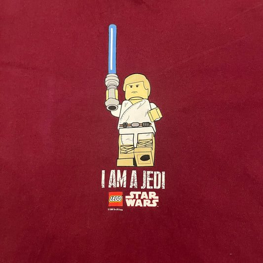 This Lego Star Wars 2008 Jedi Tee (XXXL) in burgundy showcases Luke Skywalker wielding a blue lightsaber with a 'cracked' “I Am a Jedi” text. Officially licensed by Lego Star Wars, the tee includes authentic 2008 branding under the Luke minifigure graphic.