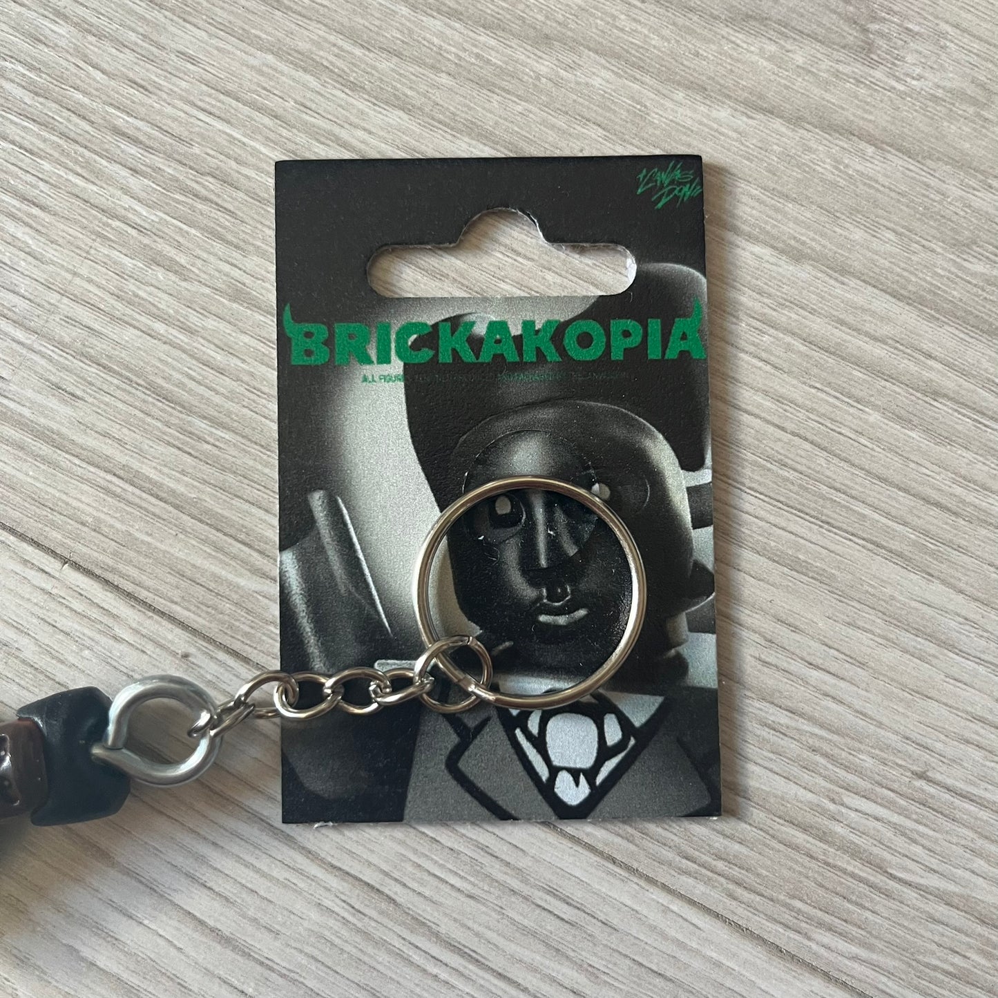 Lego x Tyler, the Creator “Brickakopia” keychain featuring a custom Lego figure of Tyler in a green suit. The figure is attached to a Lego-style recreation of the 2024 Chromakopia album cover, reimagined in brick graphics. A playful and creative collectible that merges music culture with fan-made Lego artistry, made by TheCanvasDon.