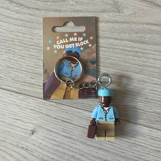 Lego x Tyler, the Creator “Call Me If You Get Block” keychain featuring a custom Lego figure of Tyler in a blue jacket with matching ushanka and suitcase. The figure is mounted on a Lego-style recreation of the 2021 Call Me If You Get Lost album cover, reimagined entirely in brick graphics. A unique collectible that blends music culture with playful Lego-inspired design, made by TheCanvasDon.