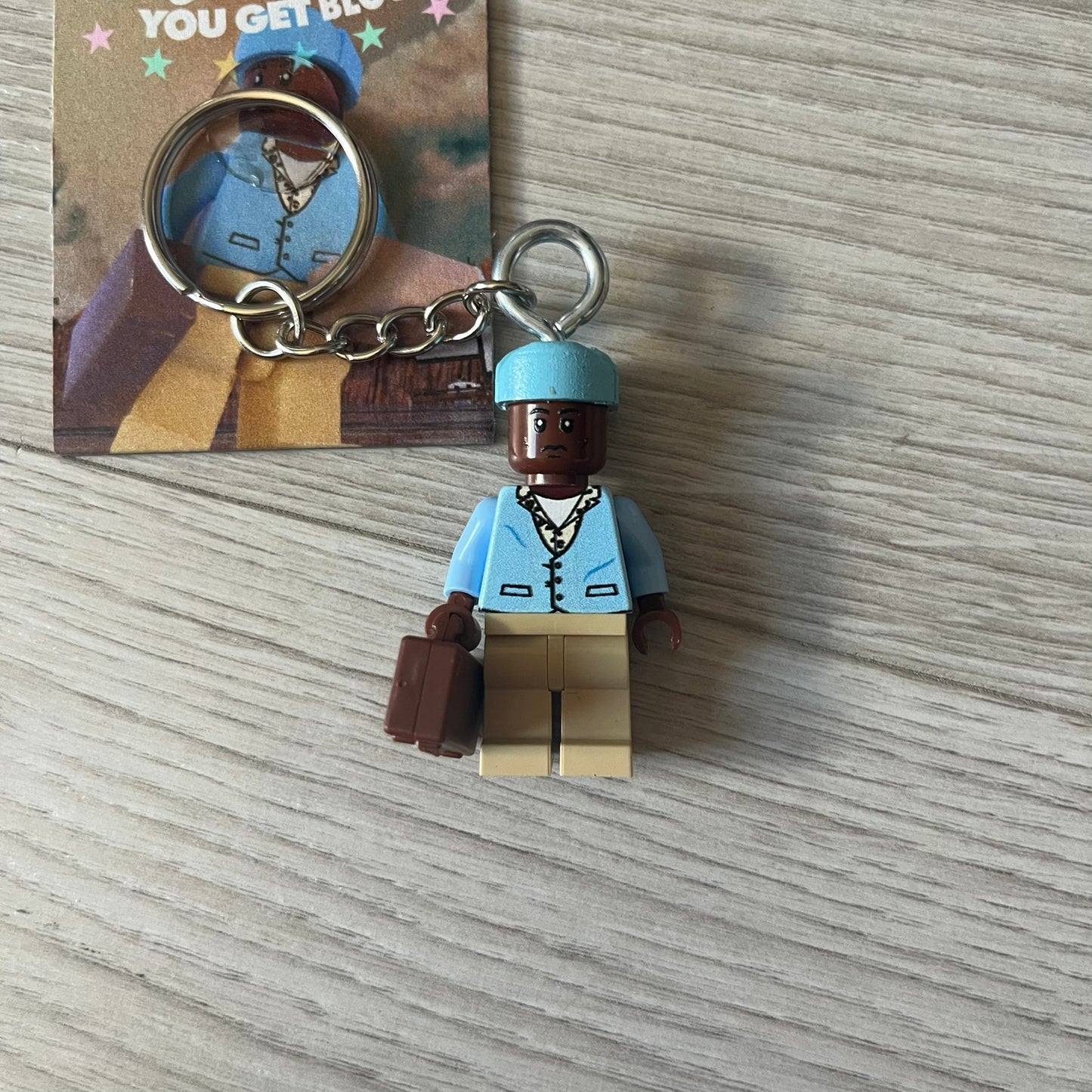 Lego x Tyler, the Creator “Call Me If You Get Block” keychain featuring a custom Lego figure of Tyler in a blue jacket with matching ushanka and suitcase. The figure is mounted on a Lego-style recreation of the 2021 Call Me If You Get Lost album cover, reimagined entirely in brick graphics. A unique collectible that blends music culture with playful Lego-inspired design, made by TheCanvasDon.