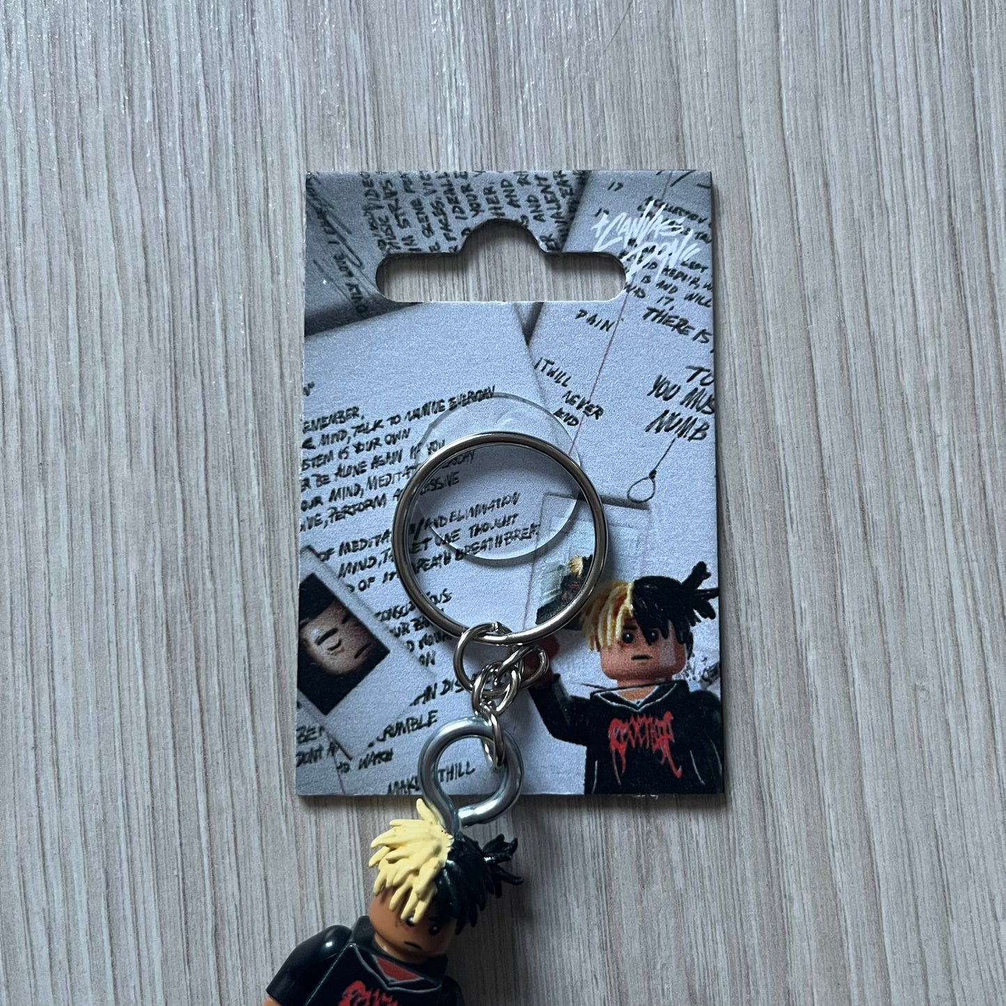 Lego XXXTentacion “XXXBlocktentacion” keychain featuring a custom Lego figure of XXXTentacion in a black/red revenge hoodie, with his classic split black and beige dreads in 3D. The figure is attached to a Lego-style recreation of the 2017 '17' album cover, reimagined in brick graphics. A great tribute and a creative collectible that merges music culture with fan-made Lego artistry, made by TheCanvasDon.