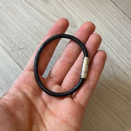 Black leather bracelet with a gold clasp held in a hand on a light wooden surface