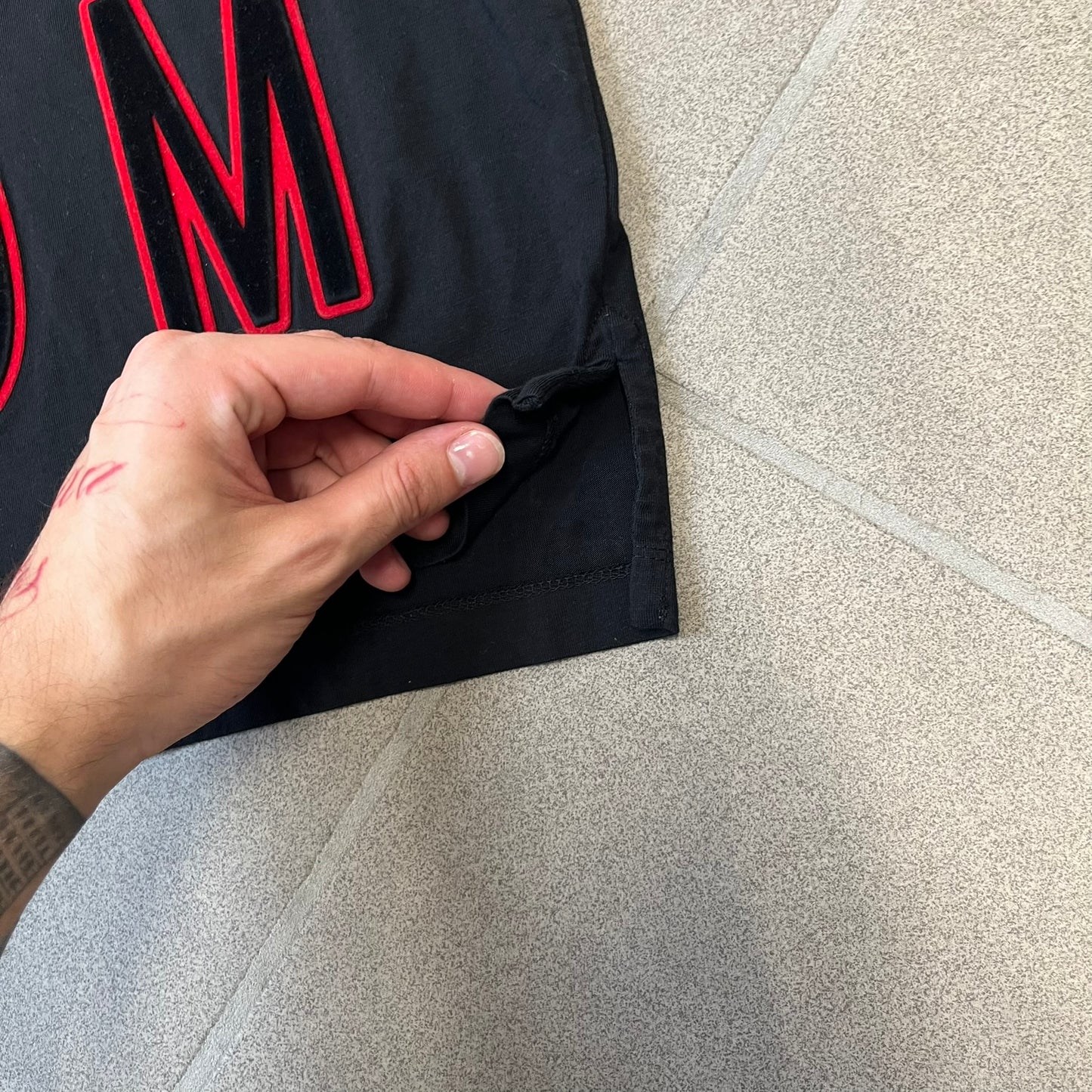 MCQ by Alexander McQueen Velvet Reverse Logo Tee features a black cropped silhouette with a slightly longer back. The front has a large black velvet MCQ logo with a red outline, accompanied by two MCQ text logos: one in the standard orientation and the other reversed as “QCM.”