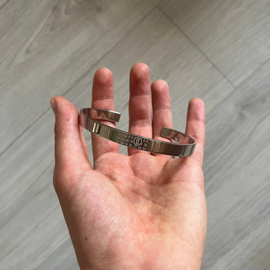 Hand holding a silver bracelet against a neutral background