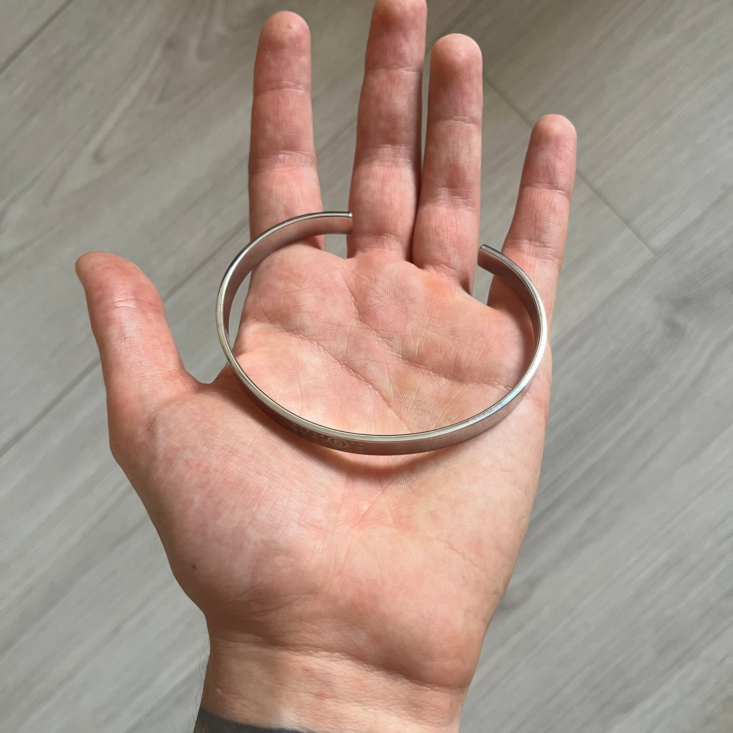 Hand holding a silver bracelet against a neutral background