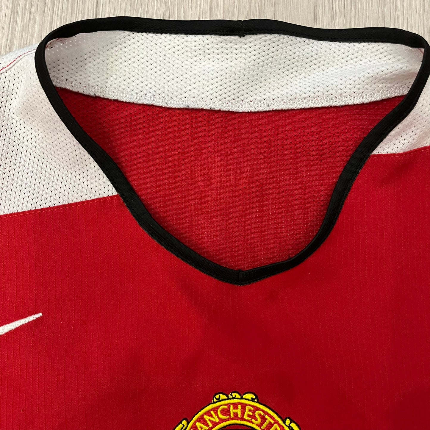 Manchester United 2004/06 Home Football T-Shirt in red, made from Nike Dri-FIT performance fabric. Features the white Vodafone sponsor logo printed across the chest, with an embroidered Manchester United crest above and a white embroidered Nike Swoosh on the right chest. Finished with white contrast detailing around the collar and sleeve hems, matching the official home design used during the 2004–2006 seasons.