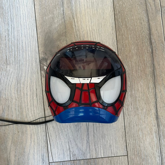 Marvel Spider-Man 2006 AM/FM Alarm Clock Radio is a digital alarm clock shaped like Spider-Man’s head with a multicolor design. It features AM/FM radio functionality and a built-in red projection display that projects the time onto a nearby surface. The clock operates using a standard 110V two-prong power connection or a 9V backup battery. All functions are fully working.