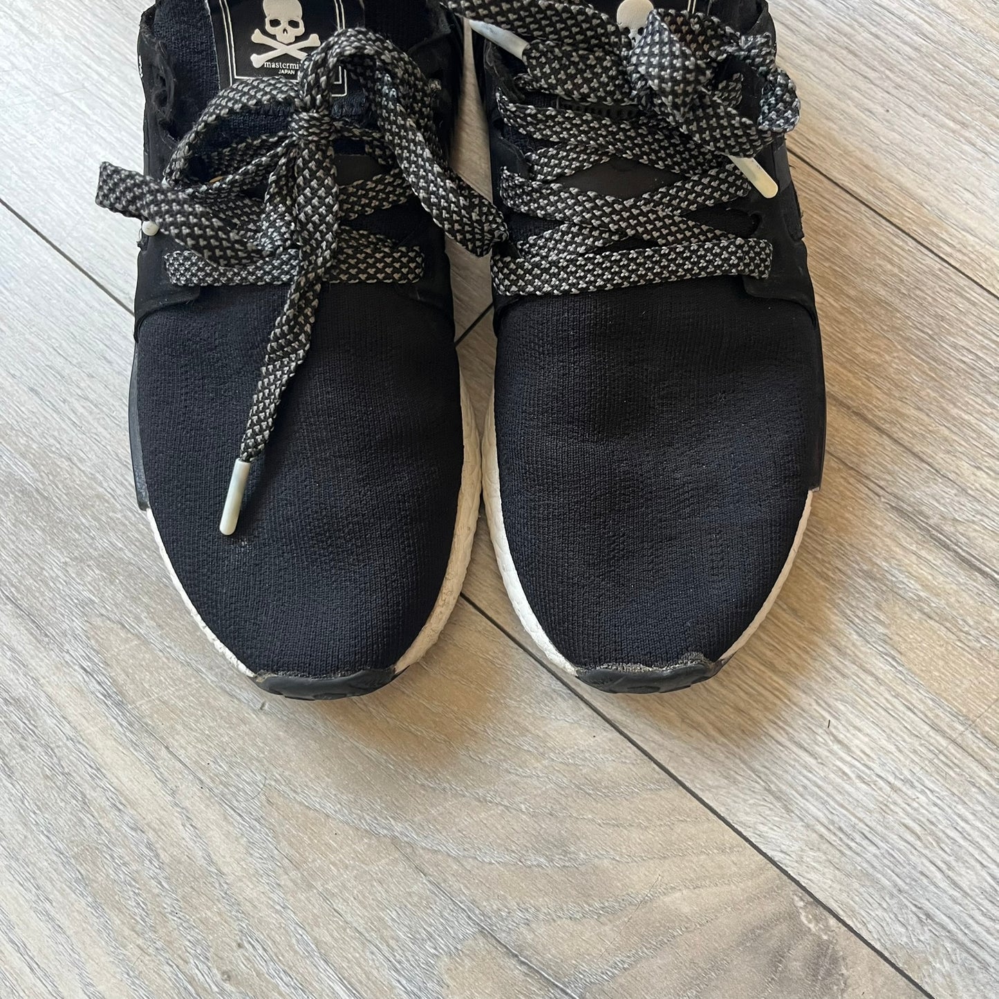 Mastermind x adidas NMD XR1 “Mastermind” Sneakers BA9726 are a 2016 collaboration between adidas and Mastermind Japan, the Japanese label founded by Masaaki Homma. The sneaker features a Core Black/Core Black/White colorway with a polyester mesh upper, rubber sole, and adidas Boost midsole. Mastermind’s signature skull and crossbones logo appears on the leather cage and tongue, while the pair includes black laces and follows the NMD XR1 silhouette released on September 20, 2016 under style code BA9726