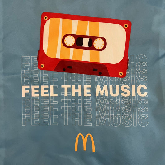 The McDonald’s Spain “Feel The Music” Backpack comes in a blue and yellow colorway with a vintage cassette graphic on the front. Constructed from lightweight non-woven synthetic fabric, it includes yellow straps and a zip-top closure. A collectible promotional item released by McDonald’s Spain.