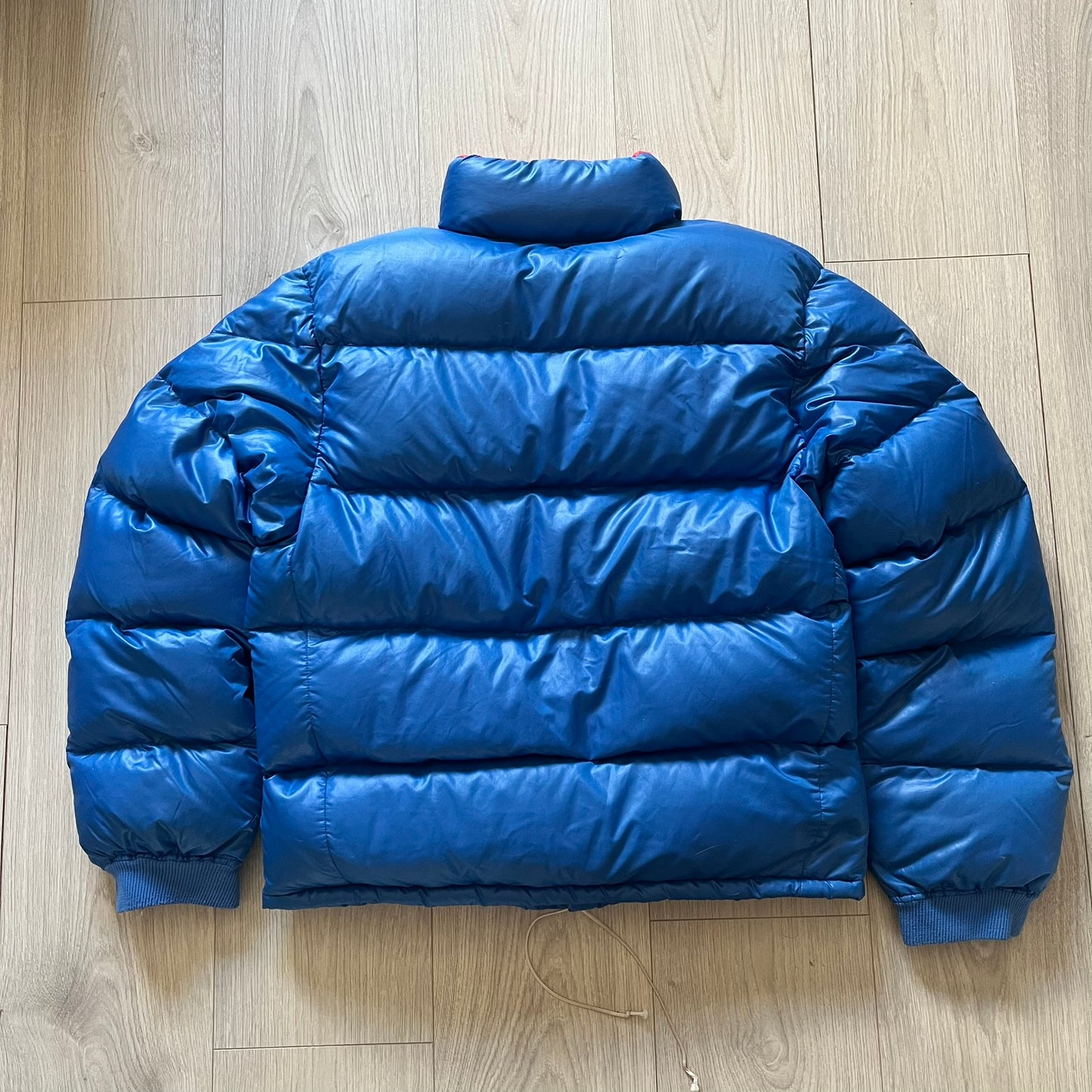 Vintage 1980s Moncler Grenoble down jacket in blue with a contrasting red lining. Features a foldable thin hood hidden in the back, silver-tone buttons and zippers, and the original Moncler patch on the sleeve. A rare French-made piece with authentic Grenoble labels, distinct from the brand’s modern ski line.