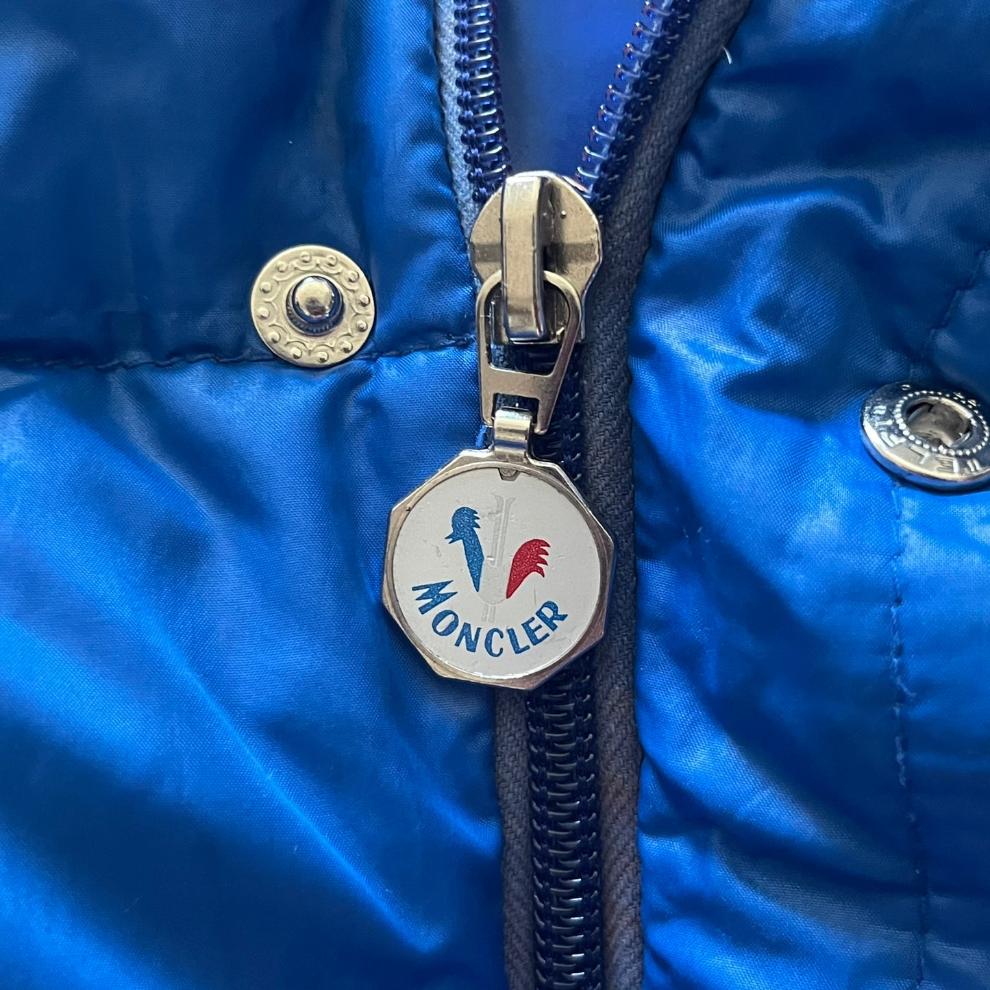 Vintage 1980s Moncler Grenoble down jacket in blue with a contrasting red lining. Features a foldable thin hood hidden in the back, silver-tone buttons and zippers, and the original Moncler patch on the sleeve. A rare French-made piece with authentic Grenoble labels, distinct from the brand’s modern ski line.