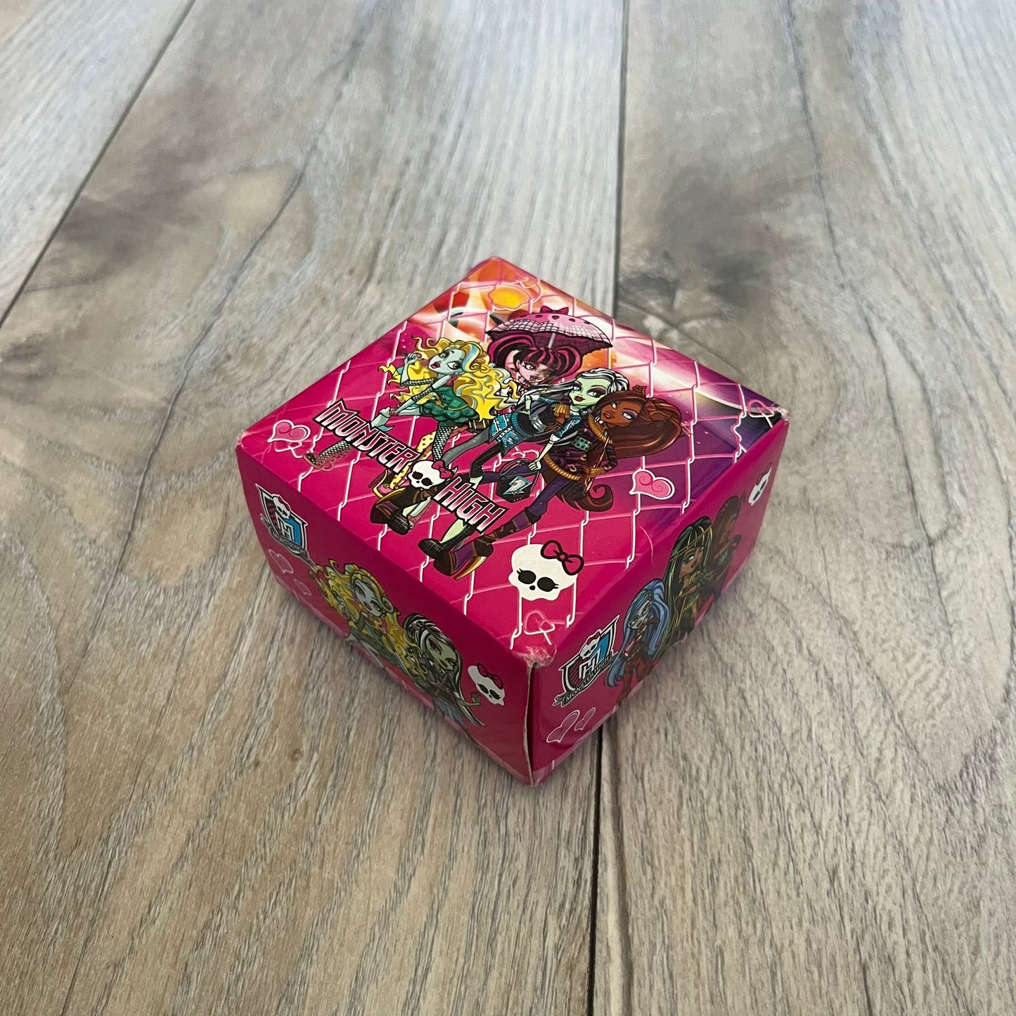 Monster High Red & Pink Kids Watch is a children’s wristwatch featuring a red strap printed with Monster High logos and character graphics. The watch has a silver-tone case with a pink dial, black numerals, and white hands, along with a Monster High character graphic and logo on the face. It comes packaged in a pink box with full Monster High branding.