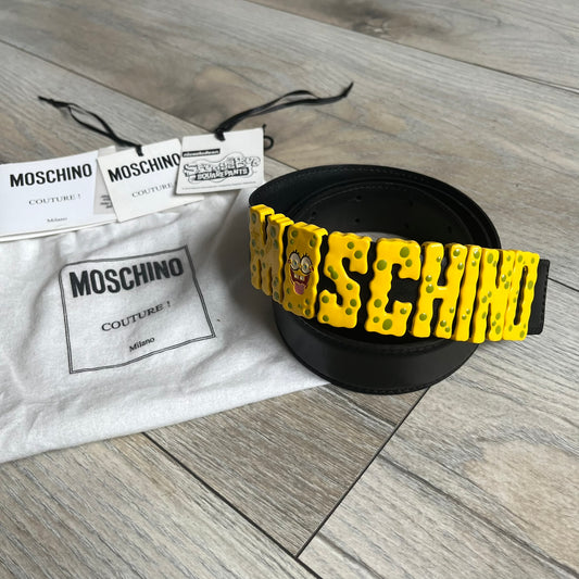 Moschino FW14 SpongeBob Leather Belt is a black leather belt from the Fall/Winter 2014 SpongeBob SquarePants collaboration. The front features the MOSCHINO logo formed by individual movable letters rather than a single rigid buckle. Each letter is finished in yellow with green sponge-like detailing, and the first “O” includes SpongeBob’s happy face. The belt uses a metal buckle closure and comes with the original dust bag and tags. Made in Italy from Genuine Leather.