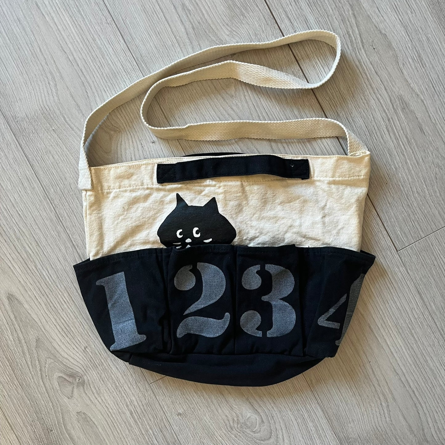 Beige bag with black cat design and number '123' on a wooden floor